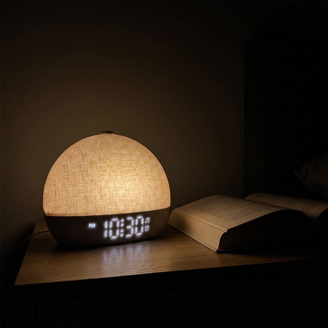 Salutive sunrise alarm clock glowing on a nightstand in a dark room